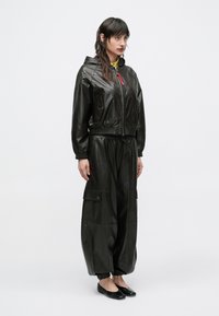 Čierna kožená bunda s kapucňou a elastickým pásom, kombinovaná s voľnými čiernymi koženými nohavicami s nákladnými vreckami a elastickými manžetami.