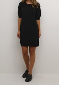 Abito nero a maniche corte con vestibilità rilassata, collo a costine e texture liscia, abbinato a mocassini neri per un look coordinato.