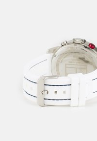 White rubber watch strap with navy stitching, featuring a metal buckle and a stainless steel watch back with two silver buttons and one red accent.