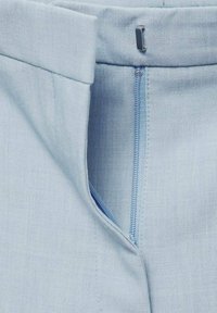 Tessuto azzurro chiaro con una superficie liscia presenta un'apertura con zip e un accento argentato in vita. Le cuciture sono ordinate e uniformi.