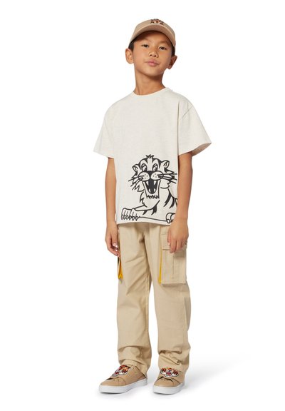 T-shirt beige avec graphique de lion noir, pantalon cargo beige avec accents de zip jaunes, et chaussures beiges avec design de lion sur le devant.