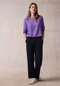 Haut long à manches violettes avec un col rond, associé à un pantalon large bleu marine et des baskets blanches. Tissu doux et coupe décontractée.