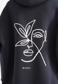 Felpa nera con design astratto di un volto e foglia ricamato in bianco sul retro. Presenta il nome del marchio "MIRONS" sotto l'opera.