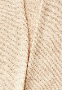 Cardigan lavorato a maglia beige con scollo a V, realizzato in un tessuto morbido che appare leggermente rigato e con un aspetto accogliente.