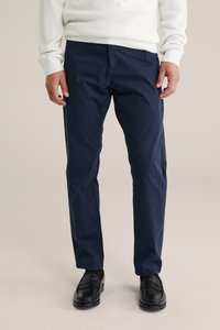 Marineblaue Chinos aus Baumwoll-Twill, gerade geschnitten, mit Vordertaschen und Gürtelschlaufen, kombiniert mit schwarzen Slip-On-Schuhen.