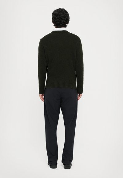 Pull en laine vert foncé avec un col rond, un ourlet côtelé et des manches longues, associé à un pantalon noir sur mesure et des chaussures noires.