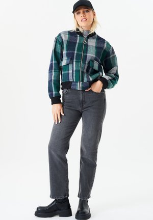Green and blue plaid cropped jacket with front pockets and ribbed cuffs, paired with gray jeans and black platform boots. Neutral background.