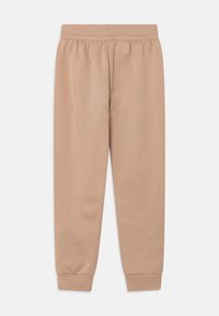 Béžové tepláky vyrobené z měkké tkaniny s elastickým pasem, zúženým střihem nohavic a žebrovanými manžetami na kotnících.