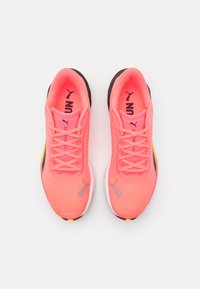 Zapatillas deportivas de malla rosa brillante con detalles en negro y amarillo, que presentan cordones planos y una suela texturizada. Logo de Puma en los laterales.