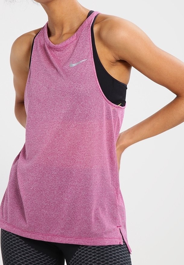 Femme portant un débardeur de sport rose sans manches avec un petit logo Nike, une brassière de sport noire en dessous et des leggings noirs à motifs.