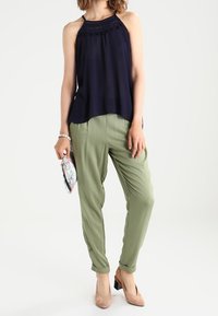 Marinblå haltertopp med avslappnad passform, kombinerad med ljusgröna avsmalnande byxor. Jordnära blockklackar och ett mönstrat kuvertväska. Mjuka tygtexturer.