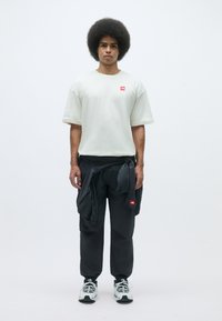 Light gray oversized t-shirt with a red logo, black pants with a logo, and black and white sneakers. Smooth fabric and relaxed fit.