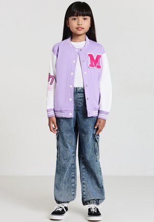 Lilafarbene Collegejacke mit weißen Ärmeln, rosa Buchstaben "M"-Patch und grafischen Details. Kombiniert mit weit geschnittenen Denim-Hosen und schwarzen Sneakern.