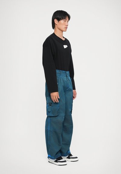 Musthave musta pika varrukaga särk ja üleliigsed sinised cargo-püksid taskutega. Tekstuuriga kangas, millel on veidi tuhm välimus. Mustad ja valged tennisajalatsid.