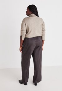 Beige turtleneck sweater with cuffed sleeves paired with dark, pinstriped wide-leg trousers. The outfit features a simple, understated design.