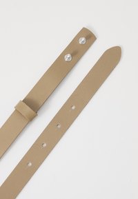 Bracelet en cuir beige avec une texture lisse, comportant deux boutons pression métalliques et plusieurs trous pour l'ajustement. Bords plats, droits, et extrémités coupées.