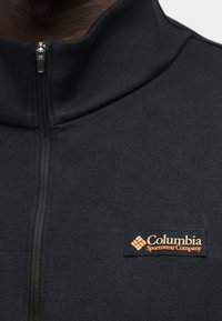 Черно яке с цип с висока яка и лого на Columbia Sportswear Company на гърдите.