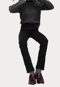 Šedý svetr s pleteným vzorem, černé džíny rovného střihu a bordó mokasíny s třásněmi, doplněné šedými ponožkami.