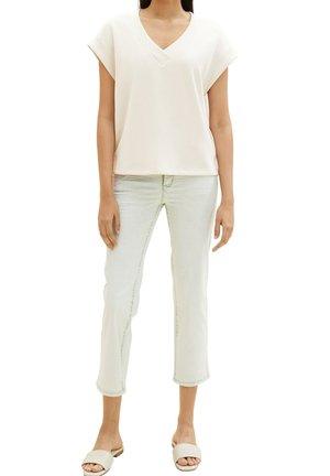 Haut blanc à manches courtes et col en V, coupe décontractée, associé à un jean court bleu clair et des sandales beige à enfiler.