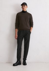 Ciemnobrązowy dzianinowy sweter, czarny golf, czarna czapka, czarne spodnie plisowane, czarne sznurowane buty. Gładka faktura, dopasowany krój, monochromatyczna kolorystyka.