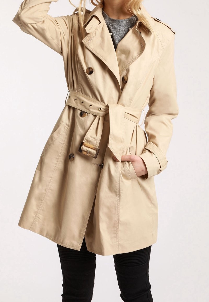 Beige trenchcoat i lättviktsmaterial med dubbelknäppta knappar, bälte i midjan och sidofickor.