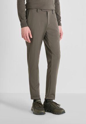Slim-fit olijfgroene broek met omgeslagen uiteinden, gedragen met bijpassende donkergroene sneakers en een lange mouwen gebreid top op een neutrale achtergrond.