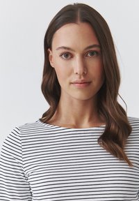 Gestreepte top in wit met zwarte horizontale lijnen, met een ronde halslijn en een gladde stof. Haar in losse golven gestyled.