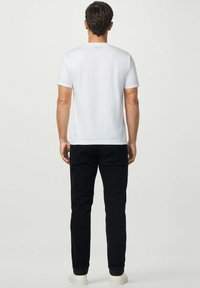 Camiseta blanca de manga corta con cuello redondo, combinada con pantalones negros ajustados y zapatillas blancas, vista desde detrás. Diseño simple y minimalista.