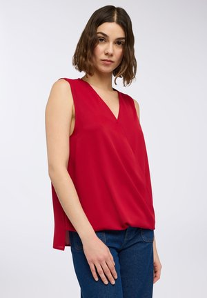 Top rosso senza maniche con scollatura a V, in tessuto fluido e vestibilità morbida. Abbinato a jeans blu, con un dettaglio a piega nella parte anteriore.