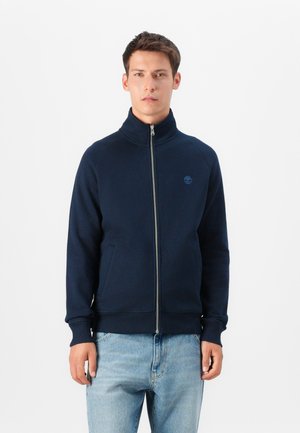 Marineblauwe ritstrui met hoge kraag, ribgebreide manchetten en twee zijzakken, gemaakt van zachte stof met een klein logo op de borst.