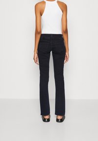 Tmavě modré, přiléhavé džíny s mírným rozšířením na spodní části, vyrobené z denimu. Zadní kapsy mají detail šití. V kombinaci s bílým žebrovaným tílkem.