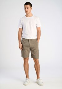 Witte t-shirt met korte mouwen gecombineerd met olijfgroene shorts tot de knie met ribbels. Model draagt witte sneakers en staat tegen een neutrale achtergrond.