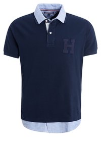 Polo bleu marine à manches courtes avec col et ourlet en couches bleu clair, présentant une lettre H bleu foncé sur le côté gauche de la poitrine.