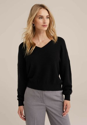 Pulover negru cu decolteu în V, cu o croială confortabilă, textură moale și mâneci lungi, asociat cu pantaloni gri, croiți atent. Design simplu și versatil.