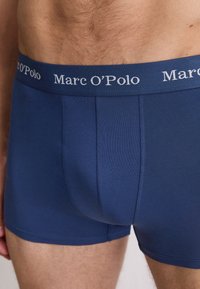 Granatowe bokserki z gładkiej mieszanki bawełny. Posiadają szeroki elastyczny pas z logo "Marc O'Polo" w jasnoszarym kolorze.