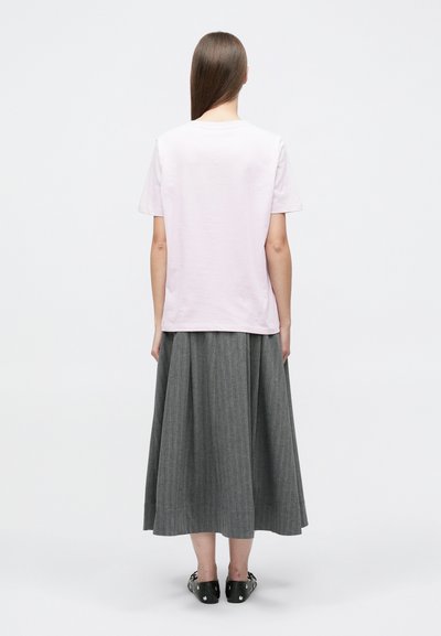 Ροζ βαμβακερό t-shirt με κοντά μανίκια, συνδυασμένο με μακριά γκρι πλισέ φούστα με κάθετες ρίγες, φορεμένο με μαύρα επίπεδα παπούτσια.