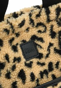 Bolso de piel sintética beige con manchas de leopardo negras, que cuenta con una superficie texturizada y una etiqueta de cuero negro grabada con "FRED BRUDER."