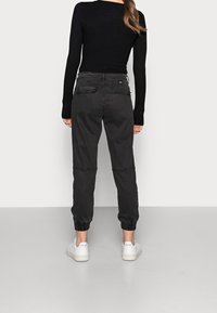 Černý proužkovaný top s dlouhými rukávy, kombinovaný s volnými šedými cargo kalhotami s elastickými manžetami a dvěma zadními kapsami. Bílé tenisky.