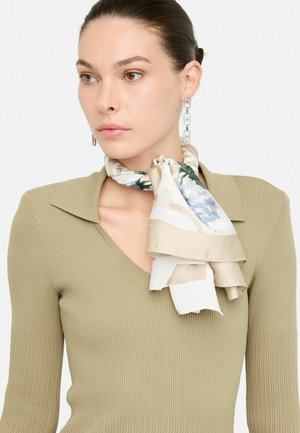 Foulard di seta con motivo floreale nelle tonalità di beige e azzurro chiaro, annodato elegantemente al collo. Top verde oliva a coste sotto.