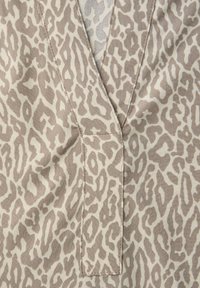 Tissu beige avec imprimé animal taupe, col en V et poche discrète, présentant une texture lisse et des coutures nettes.