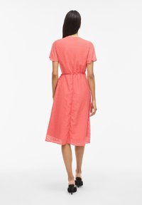 Korálové midi šaty s krátkymi rukávmi, so vzorom v tvare chevron a opaskom v páse. Ľahká, polopriesvitná tkanina s voľným strihom.