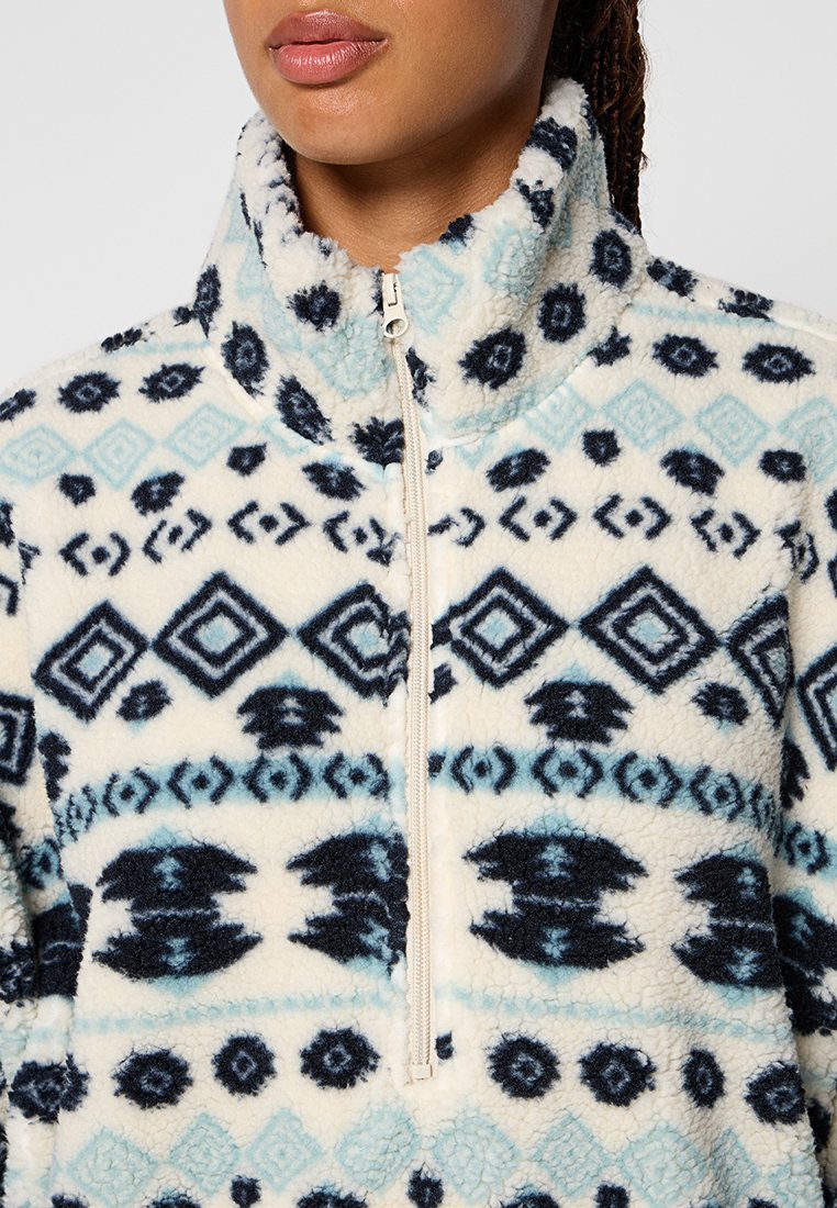 Pull en polaire avec col montant, fermeture éclair et motif géométrique en bleu marine, bleu clair et crème. Tissu doux et texturé.