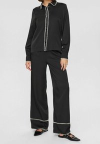 Black blouse with white contrast stitching and buttons, paired with black wide-leg pants featuring a white trim at the hem.