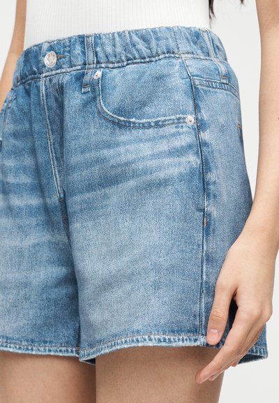 Short en denim avec un lavage bleu clair, taille élastique, poches avant et coupe droite. Le tissu a une apparence douce et texturée.