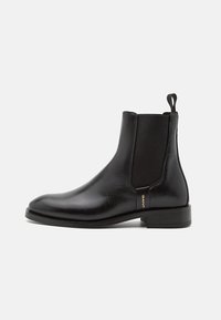 Schwarzer Chelsea-Stiefel aus Leder mit elastischen Seitenteilen, abgerundeter Spitze und einem Zuglasche. Verfügt über einen niedrigen, gestapelten Absatz und dezente goldene Markenkennzeichnung.