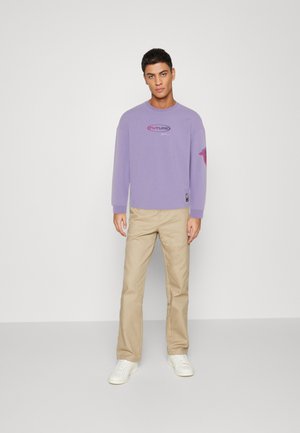 Purple long-sleeve sweatshirt with "FUTURE" logo on the chest, paired with beige pants and white sneakers, on a neutral background.