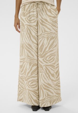Persoană purtând pantaloni largi cu imprimeu de zebra în nuanțe de bej și crem, cu talie cu șnur, și pantofi negri cu vârf pătrat.
