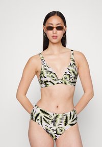 Conjunto de biquíni com um decote profundo e calções de cintura alta. O tecido é estampado com folhas tropicais verdes e pretas sobre um fundo rosa claro.