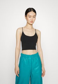Top cropped preto com alças finas, combinado com calças largas de cintura alta em tom teal, feitas de um material brilhante.