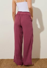 Wijdvallende broek van zacht mauve stof, met een gestructureerde tailleband, zijzakken en een vloeiend ontwerp. Soepele textuur met een lichte glans.